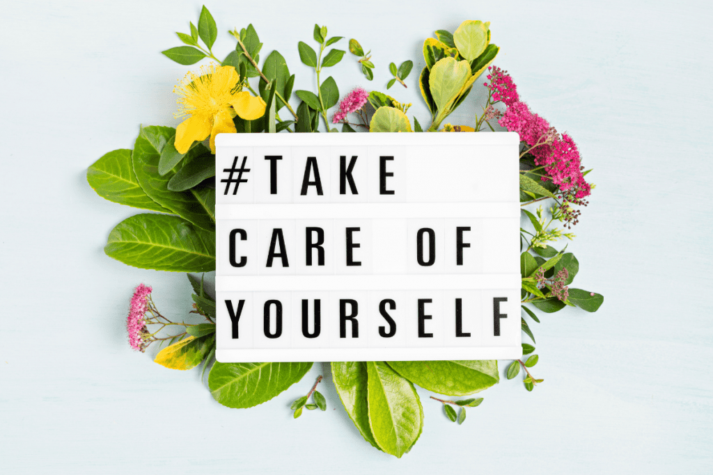 sign with words #take care of yourself surrounded by flowers on a white background