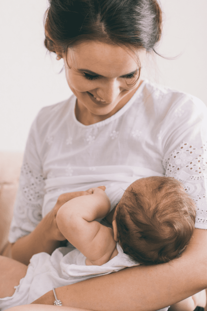 mom with brown hair and white shirt nurses her small dark haired baby
