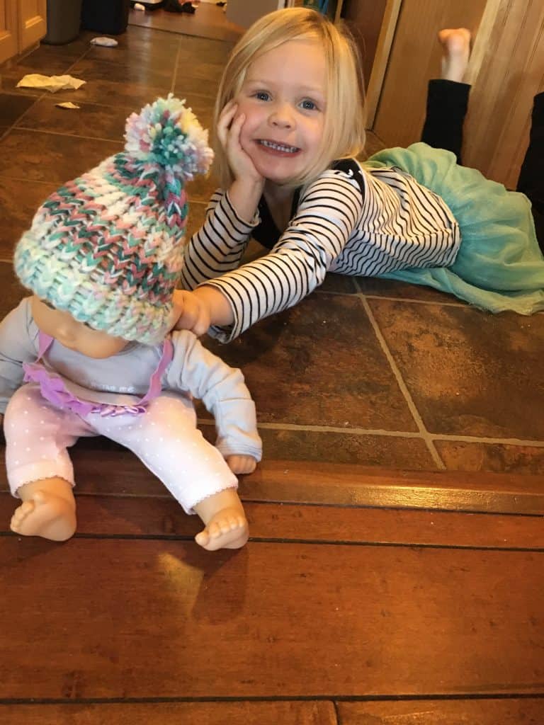 preschool girl holds out bitty baby dressed in winter hat