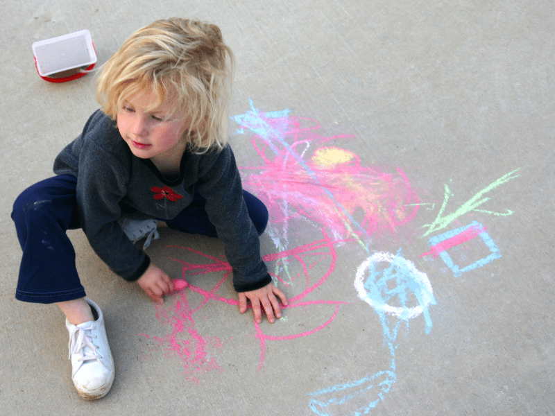 Toddler with messy blonde hair plays with brightly colored sidewalk chalk