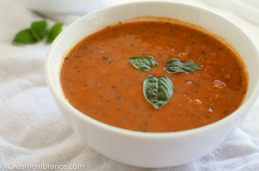 white Bowl of tomato soup with basil leaves on a white background 