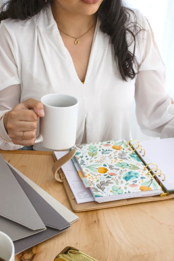 brunette woman in white robe sitting at table journaling while drinking coffee
