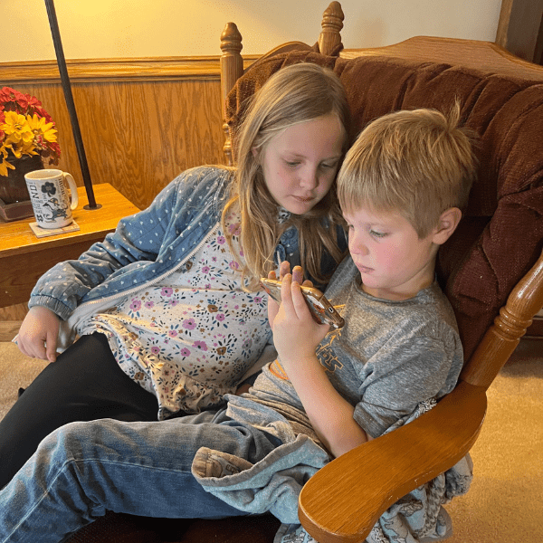 two elementary age kids with blonde hair sit in a rocker playing with homer learning app