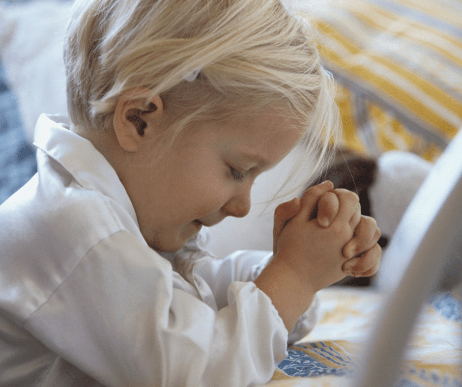 child with blonde hair and white shirt prays with folded hands
