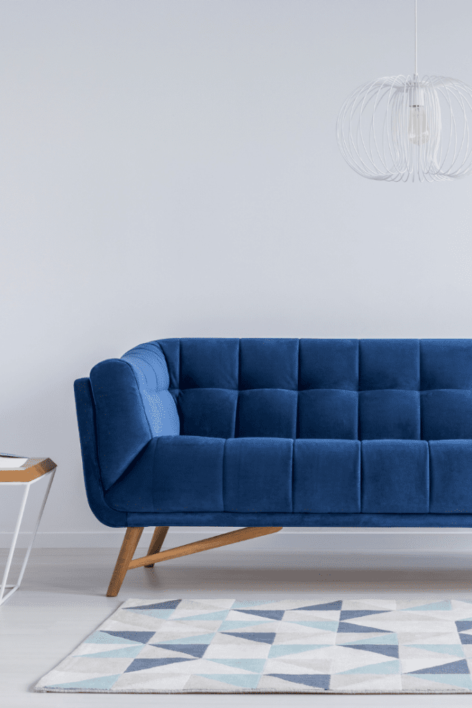 blue midcentury couch with small end table beside and blue and white rug in front of it