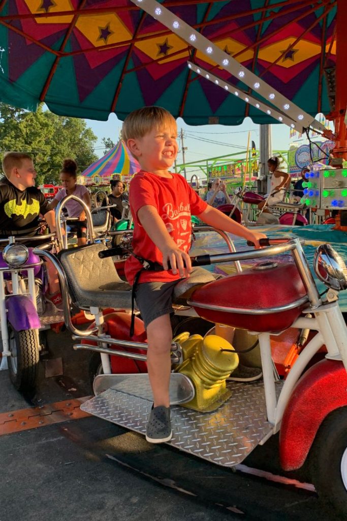 Young boy rides a motorcycle at amusement park during summer