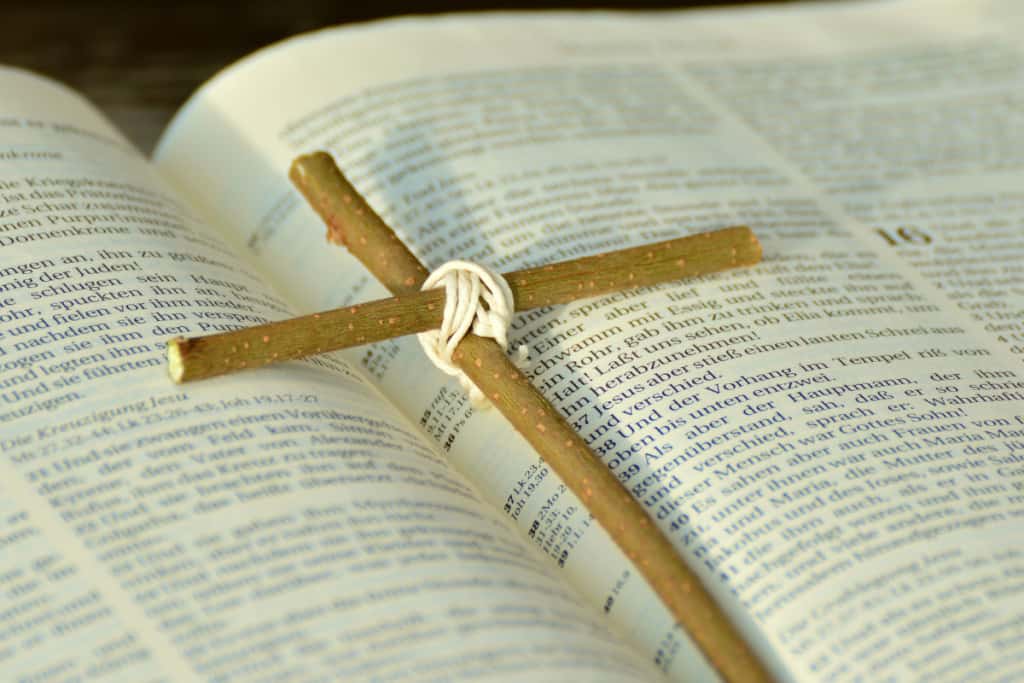 wooden stick cross tied with rope lays on an open Bible