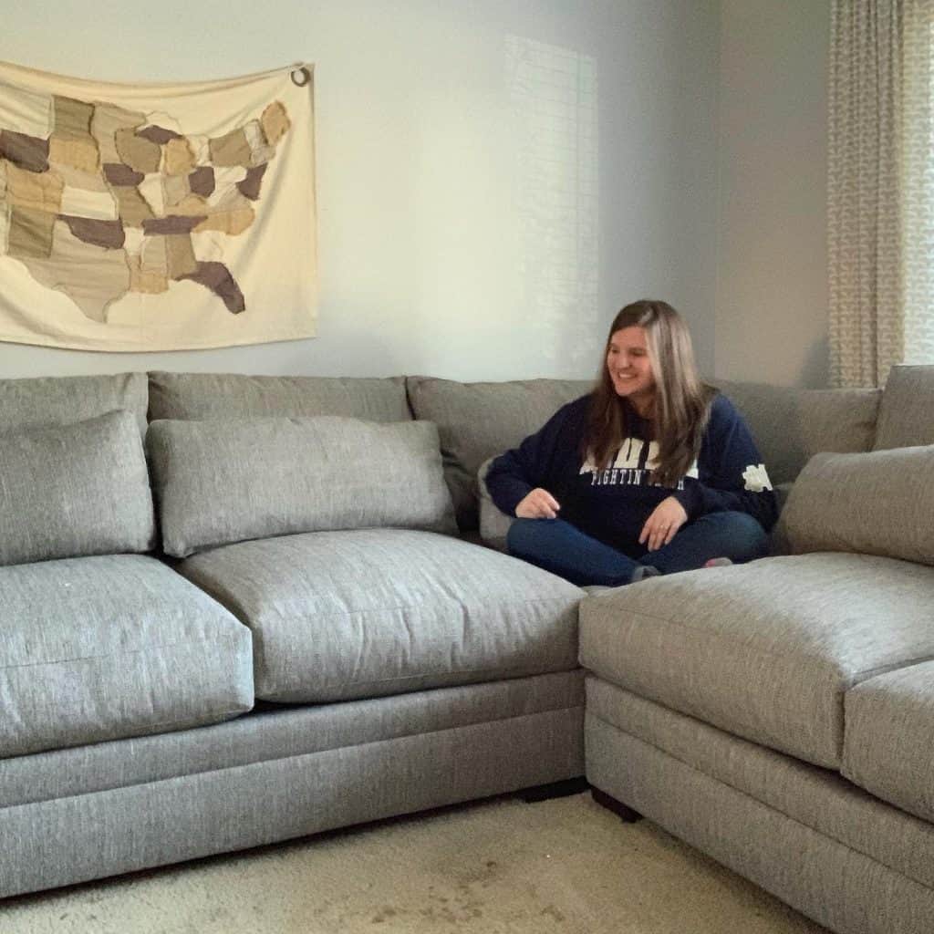 a woman in a notre dame sweatshirt sits smiling on the corner of a large sectional