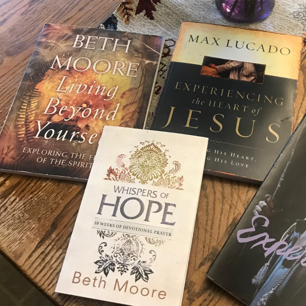Some older Beth Moore Bible studies alongside a Max Lucado Bible study lie on a Amish style table