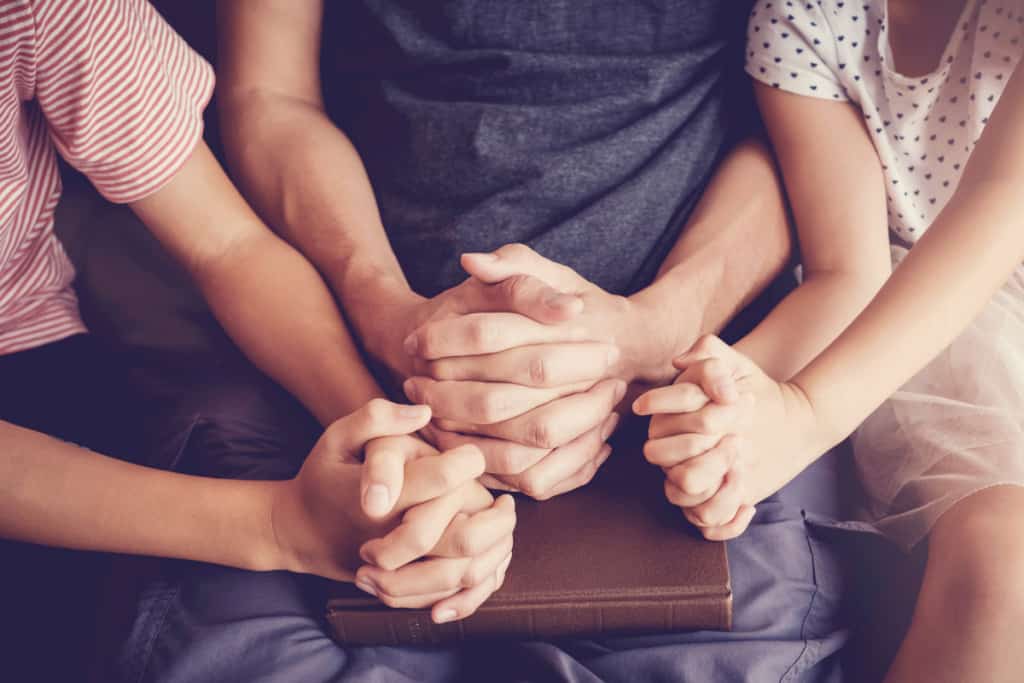 woman holding hands and praying with her children