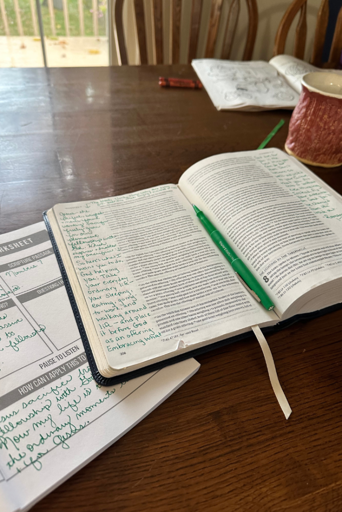 Open Bible and Bible study notes on a kitchen table with pink coffee mug and window in background