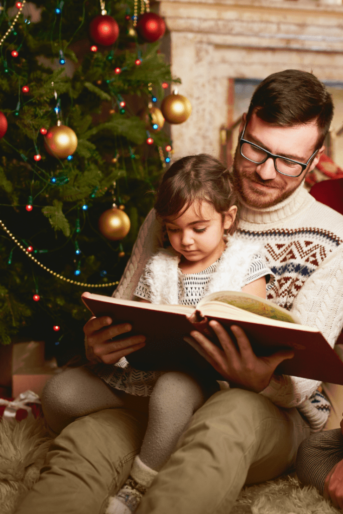 dad reads Bible to daughter sitting under Christmas tree