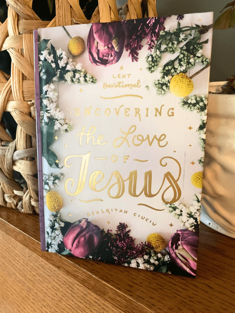 Book, Uncovering the Love of Jesus: a Lent devotional with floral cover leans against an open weave basket in the sunshine