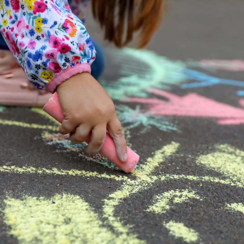 small child's hand reaches to complete a chalk stick figure on a driveway art exhibit