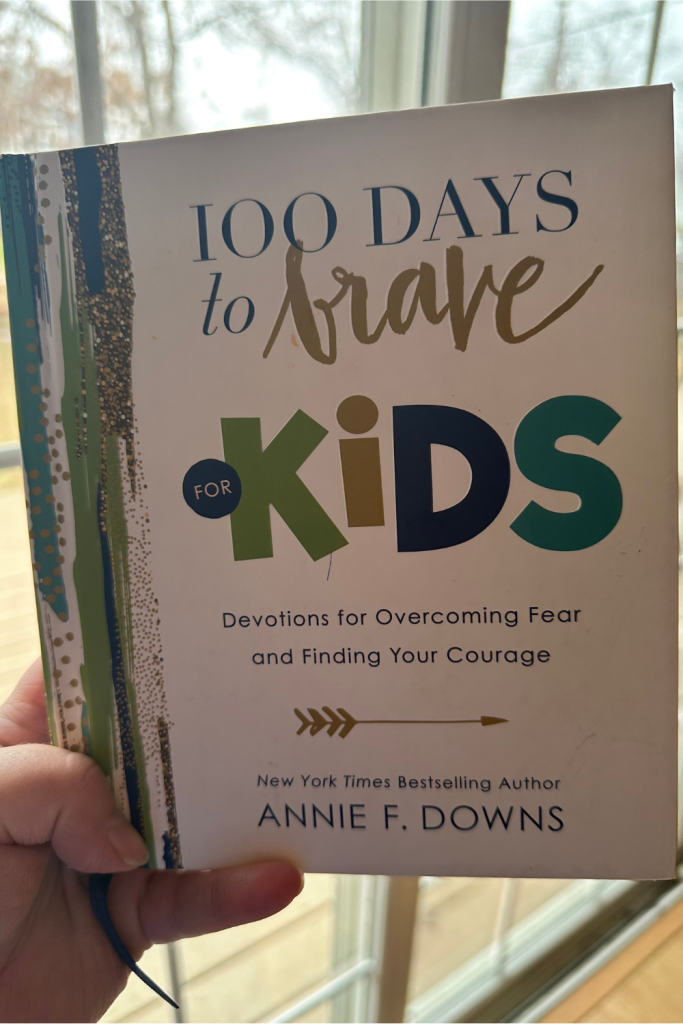 100 days to brave devotional book for kids by annie f downs held up near a window