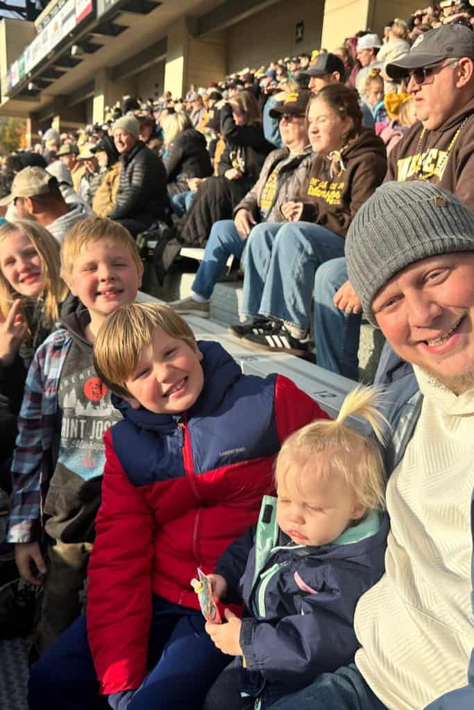 fall bucket list activity: attending a college football game. A family sits in the stands of a Western Michigan football game with big smiles on their faces