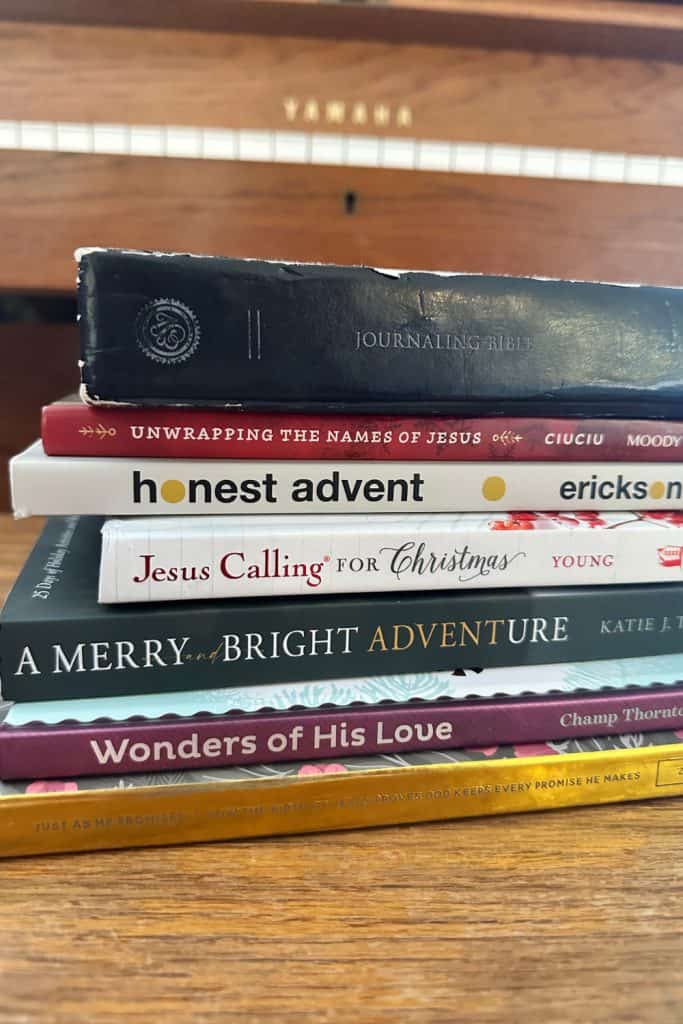 Stack of adult Christmas devotionals on a piano bench with a Bible on top.