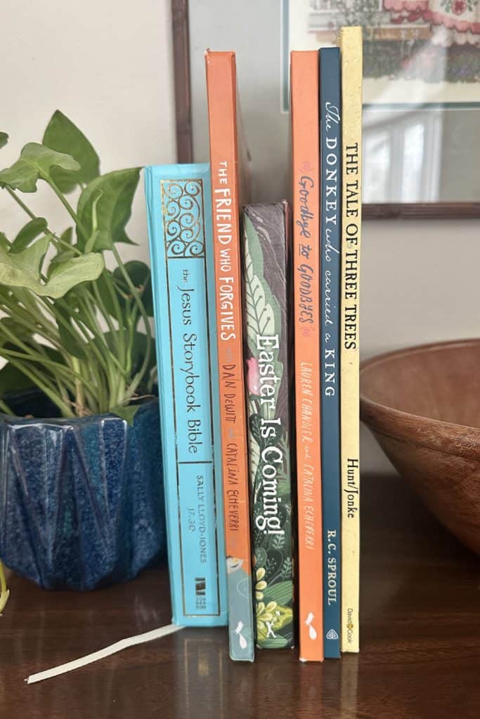 Christian Easter books for kids on a shelf beside a plant and a wooden bowl