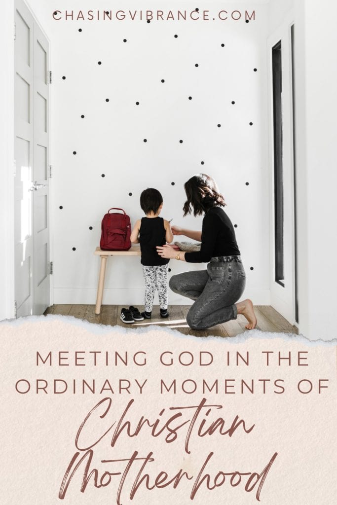 woman kneels with her small son helping him get readymade while "meeting god in the ordinary moments of christian motherhood"
